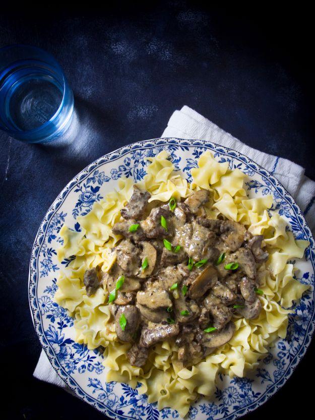 Blue and white patterned plate of egg noodles topped with beef stroganoff and mushrooms on a dark background