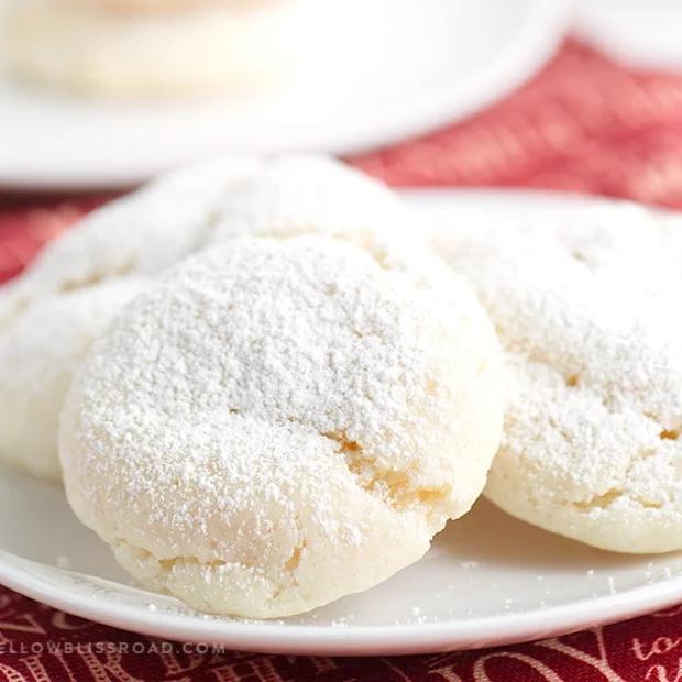 Soft white snowball cookies dusted thickly in powdered sugar on a white plate over a red holiday napkin