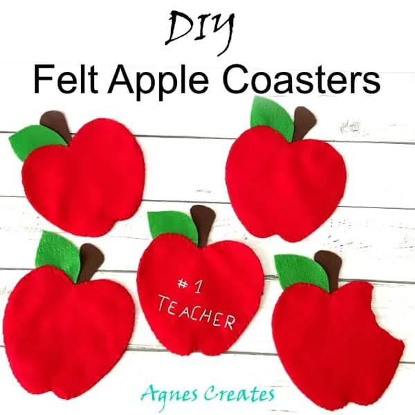 Five red felt apple coasters with green leaves and brown stems on white wood, one embroidered number one teacher, one bitten