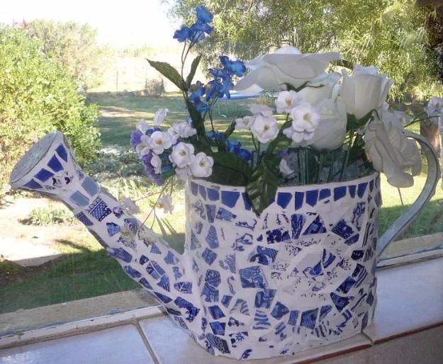 Mosaic watering can covered in blue and white willow pattern china pieces, filled with white and blue flowers by a window