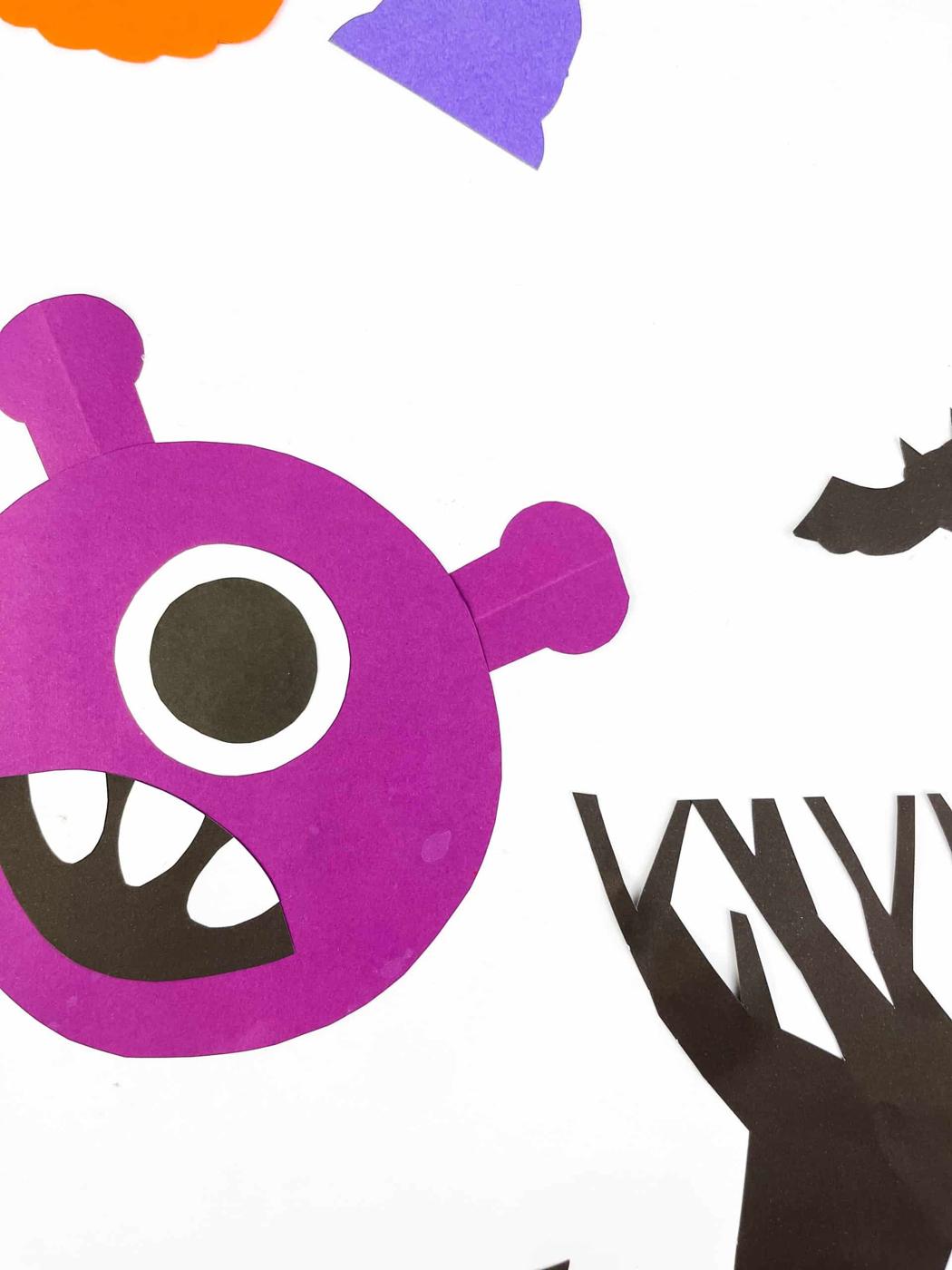 Purple one-eyed paper rocking monster with black mouth, white teeth and paper horns against a white background