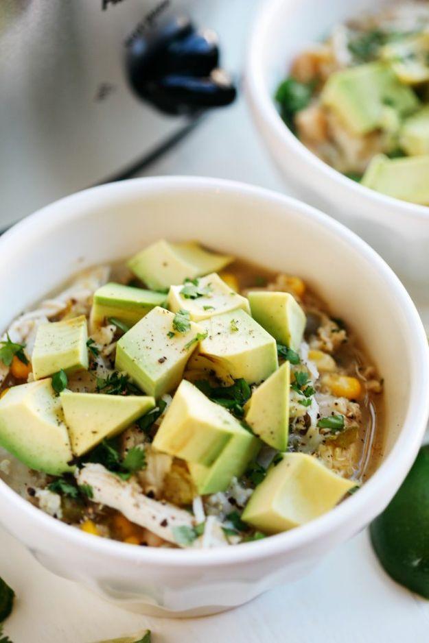 White chicken and quinoa chili in a white bowl topped with large chunks of fresh avocado and cilantro