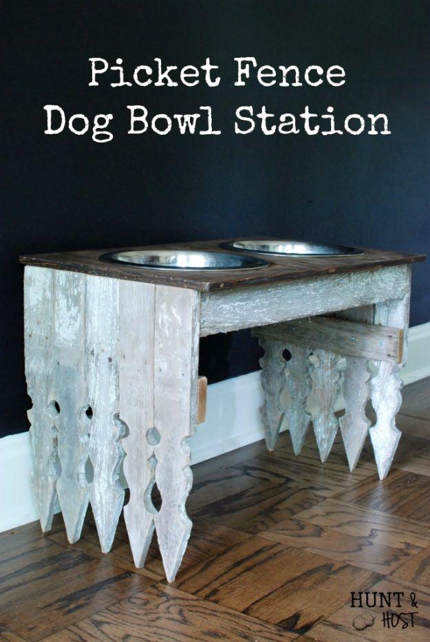 A raised dog feeding station built from weathered fence pickets holds two steel bowls on a kitchen floor