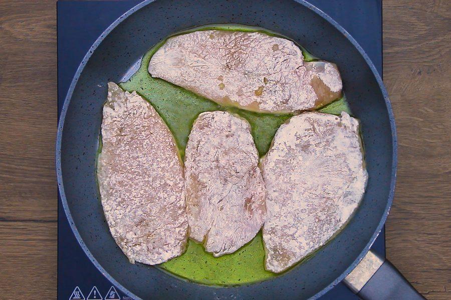 Four floured chicken cutlets pan frying in olive oil in a skillet for an easy chicken piccata dinner