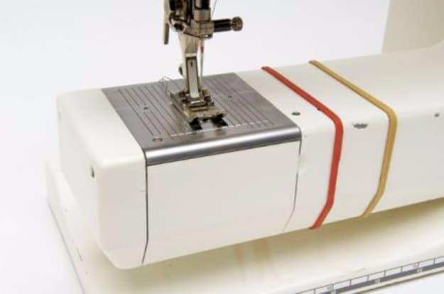 A sewing machine free arm with red and tan rubber bands stretched around it as seam allowance guides