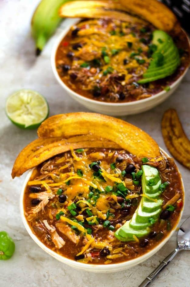 Jamaican jerk chicken chili in two bowls topped with fried plantain chips, avocado slices and fresh lime