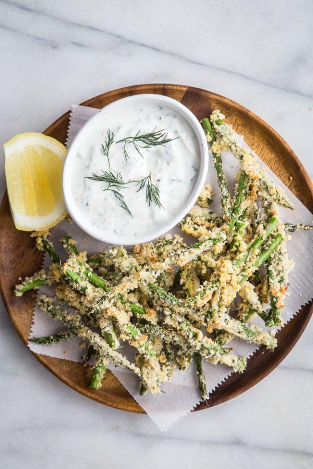 Crispy asparagus fries on a wooden board with breaded spears and a bowl of creamy lemon dill dipping sauce