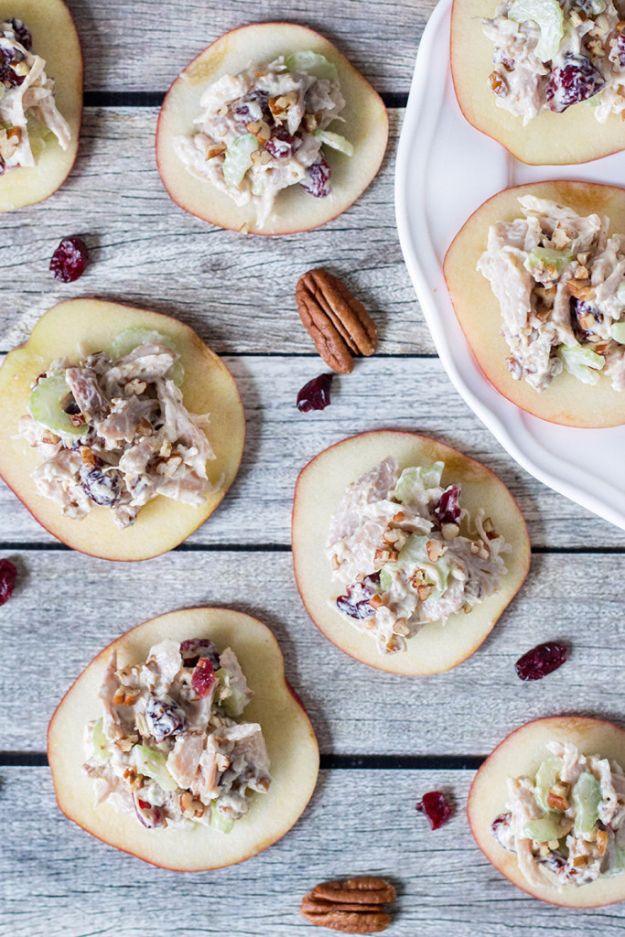Cranberry chicken salad spooned onto thin apple rounds with scattered dried cranberries and pecans on pale wood