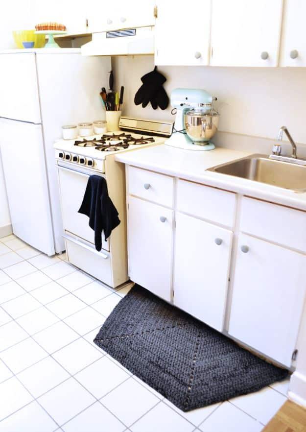 Dark grey half hexagon DIY crochet rug in chunky t-shirt yarn on white tile in front of white kitchen cupboards