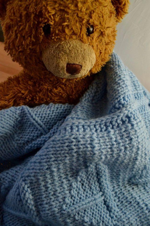 Soft blue textured knit baby blanket draped over a large brown teddy bear, folds showing the fabric depth