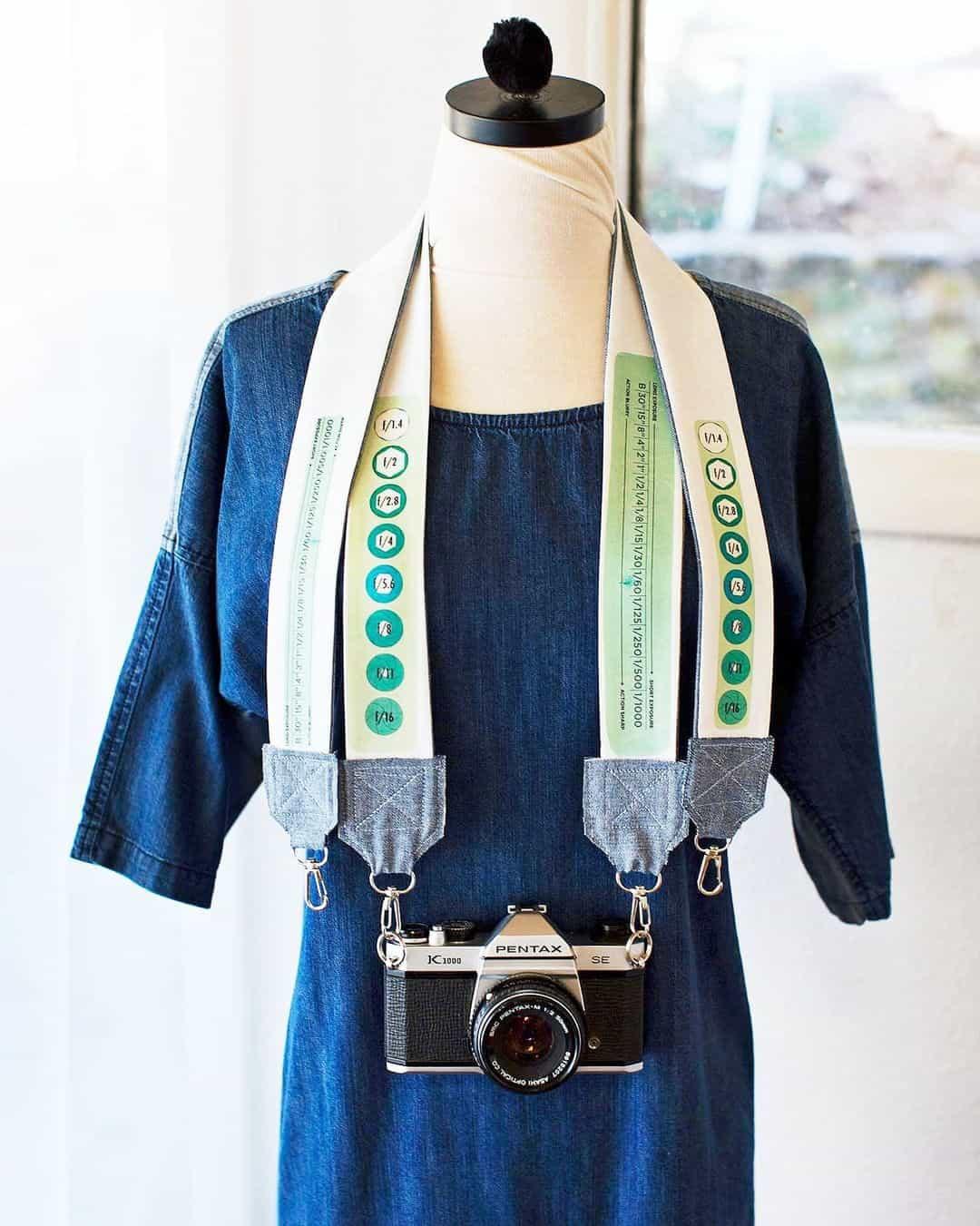DIY camera strap sewing idea, a cream printed strap with gray tabs holding a vintage camera on a dress form