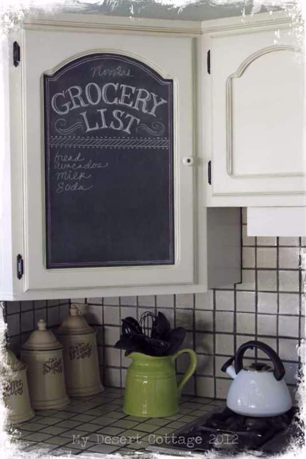 Kitchen cabinet door fitted with a black chalkboard panel lettered with a grocery list, above a tiled backsplash