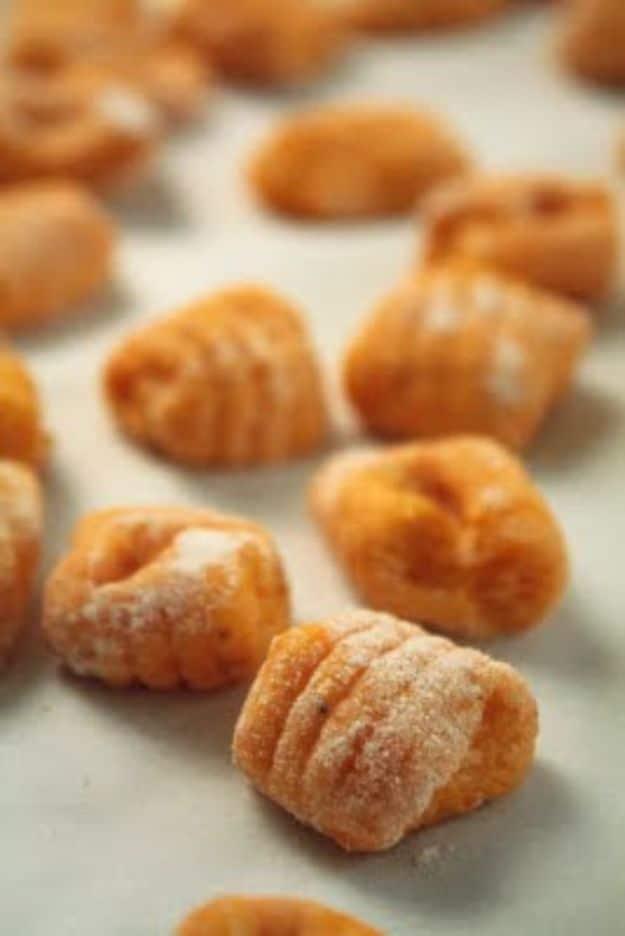 Uncooked butternut squash gnocchi dusted with flour, scattered and spaced loosely on a pale work surface