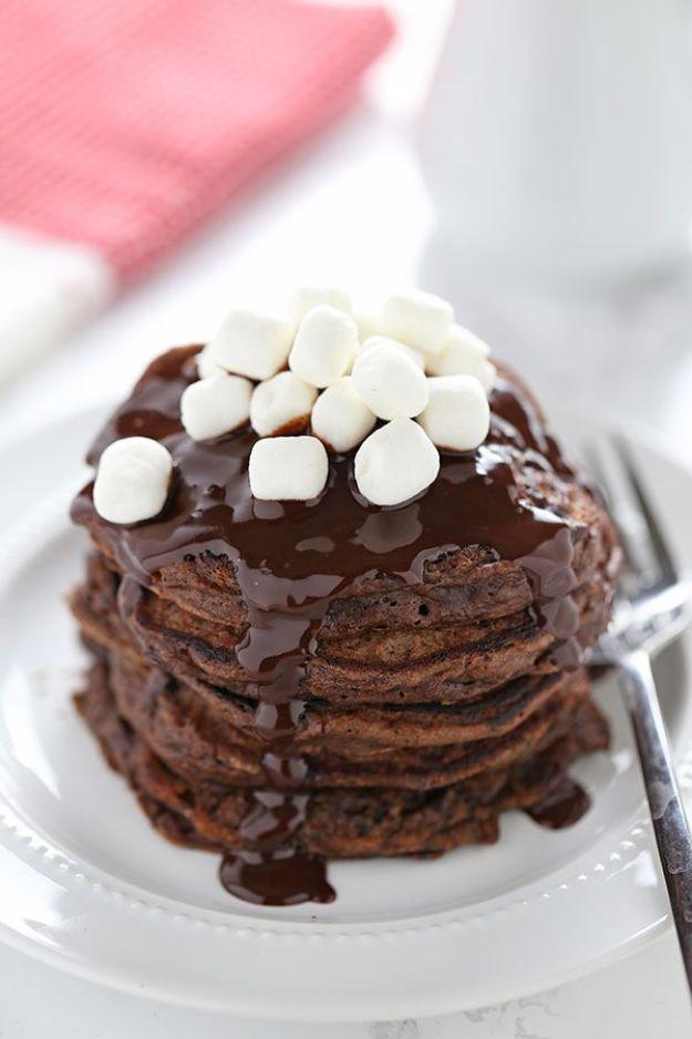 Hot chocolate pancakes stacked and covered in dark fudge sauce with mini marshmallows piled on the top