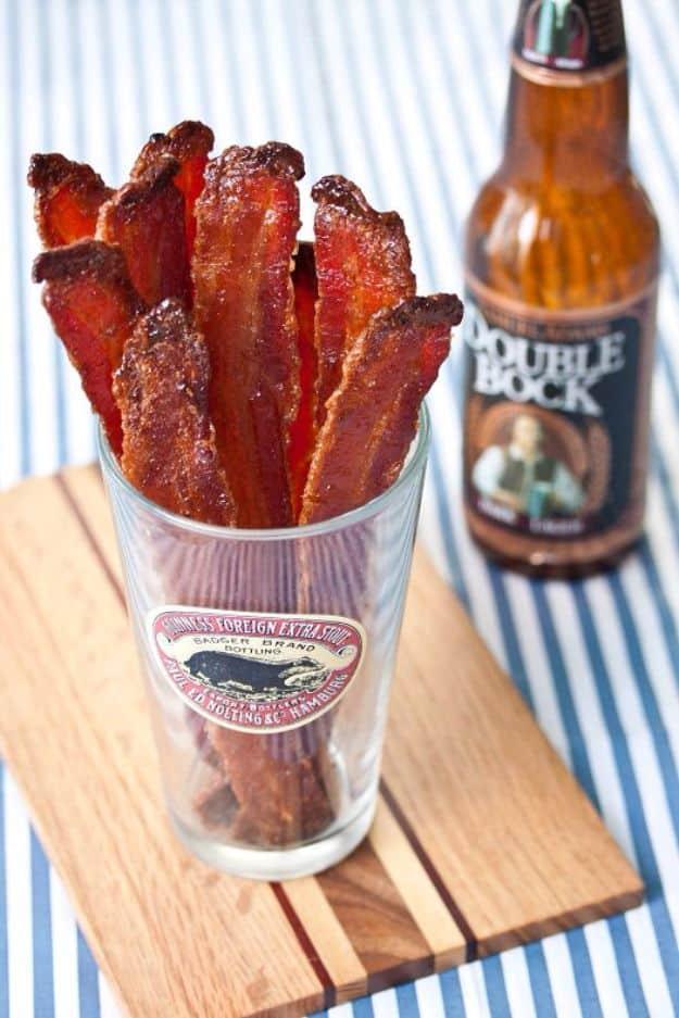 Beer-candied bacon standing upright in a pint glass on a wooden board, a Double Bock bottle behind it
