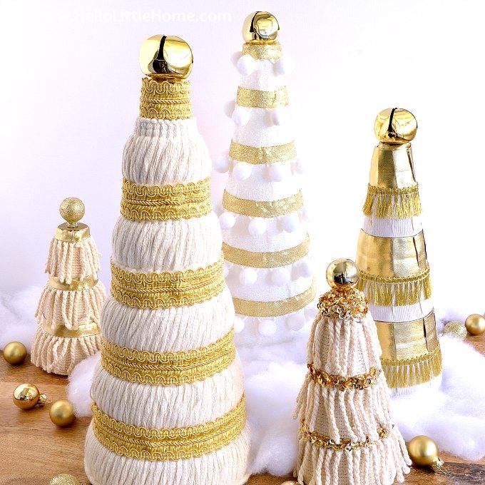Five cream and gold cone trees wrapped in yarn, ball fringe, gold braid and sequin trim with jingle bell toppers in faux snow