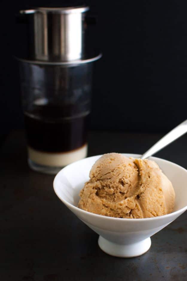 Vietnamese coffee ice cream scooped into a white bowl beside a metal phin filter dripping over a glass