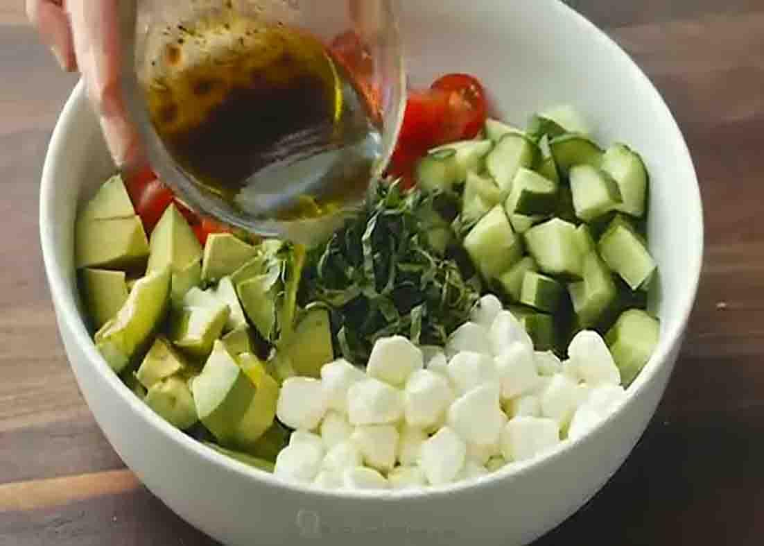 Drizzling the dressing for the tomato cucumber mozzarella salad