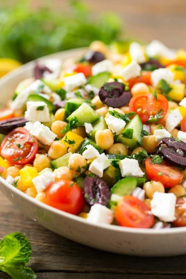 Chopped Greek salad in a white bowl with cucumber, chickpeas, cherry tomatoes, kalamata olives and feta