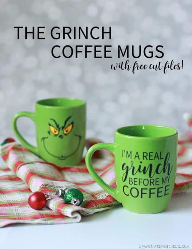 The Grinch coffee mugs, two green mugs with a Grinch face decal and lettering, on a striped cloth with ornaments