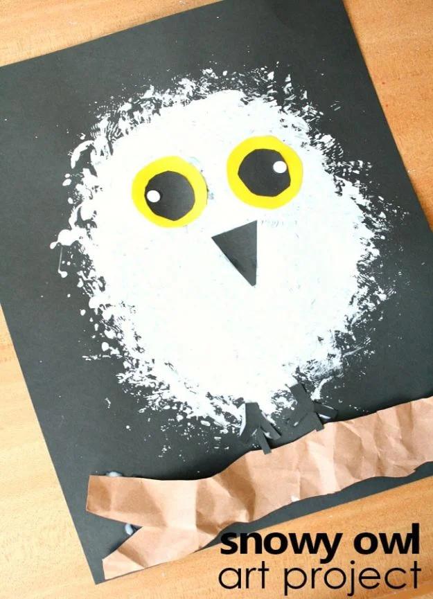 White loofah stamped snowy owl on black paper with round yellow eyes and a black beak standing on a torn brown paper branch