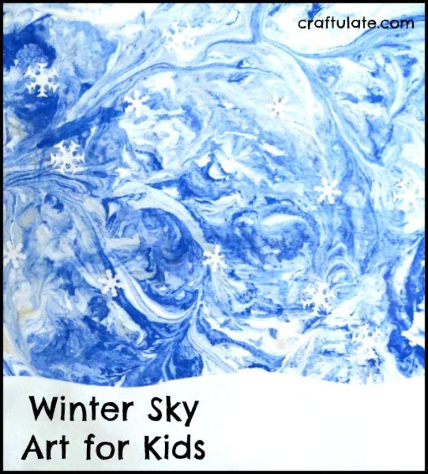 Blue and white shaving cream marbled sky scattered with small punched paper snowflakes, labeled craftulate.com