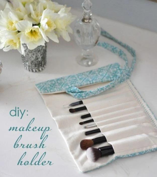 Makeup brush holder, a cream fabric roll with aqua trim holding a row of brushes, daffodils in a silver vase behind