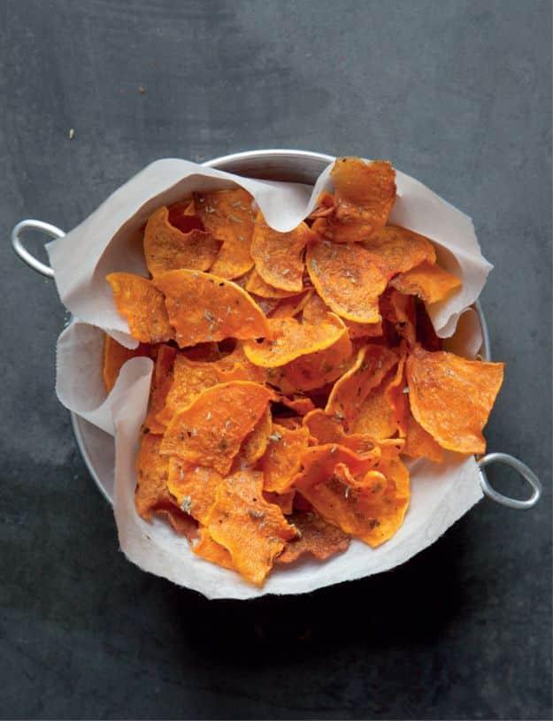 Butternut squash veggie chips piled in a white bowl lined with parchment paper on a dark stone background