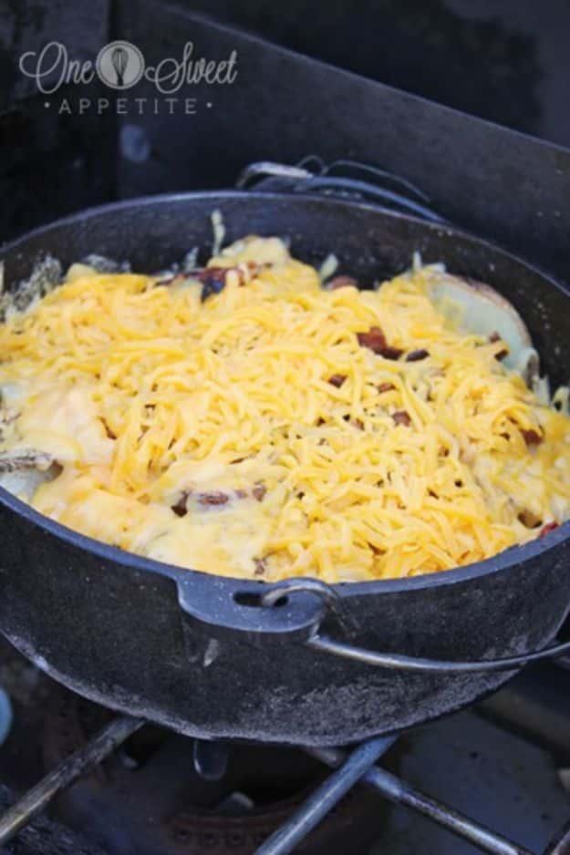 Cheesy dutch oven potatoes layered with bacon, sliced onions and shredded cheese, cooked over hot coals