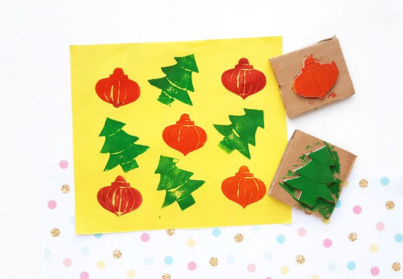 A yellow sheet printed with red bauble and green tree shapes beside two handmade foam and cardboard stamps