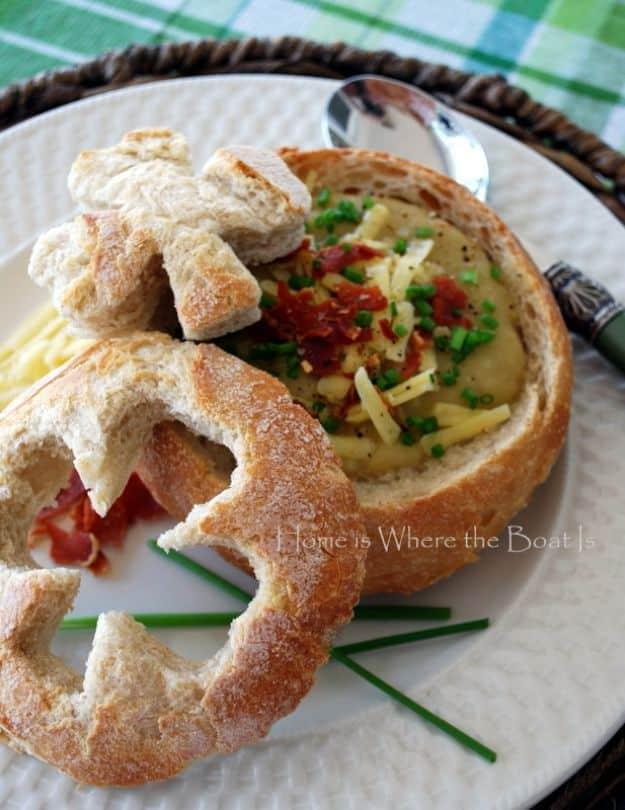 Irish potato soup served in a round bread bowl with shamrock shaped bread cutouts, bacon, cheese and chives
