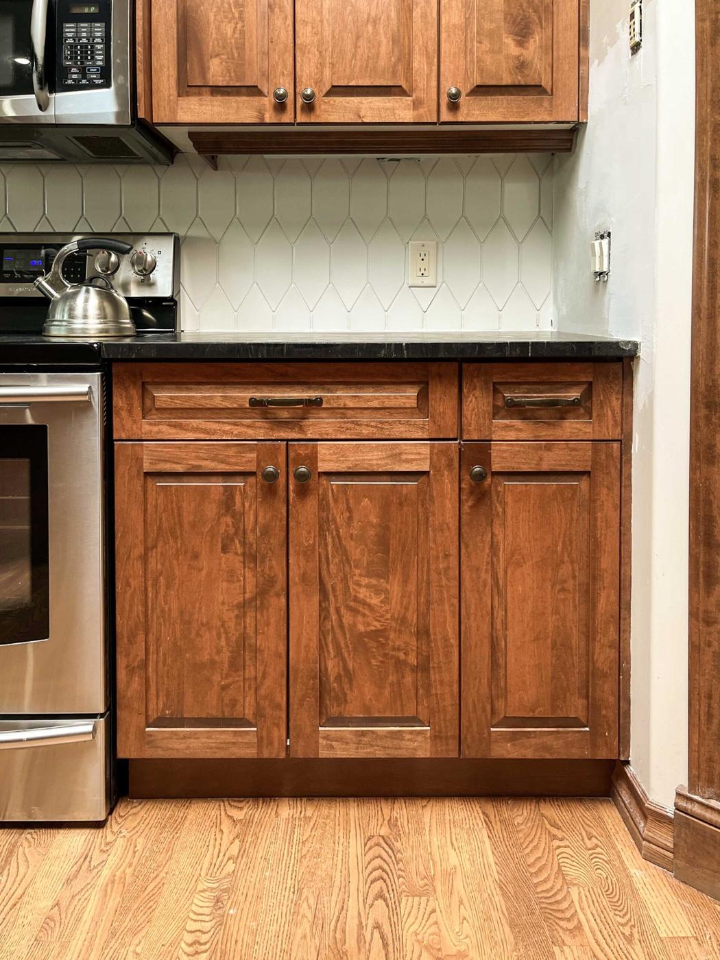 White elongated hexagon tile backsplash behind warm wood cabinets with a black counter and a stainless steel range