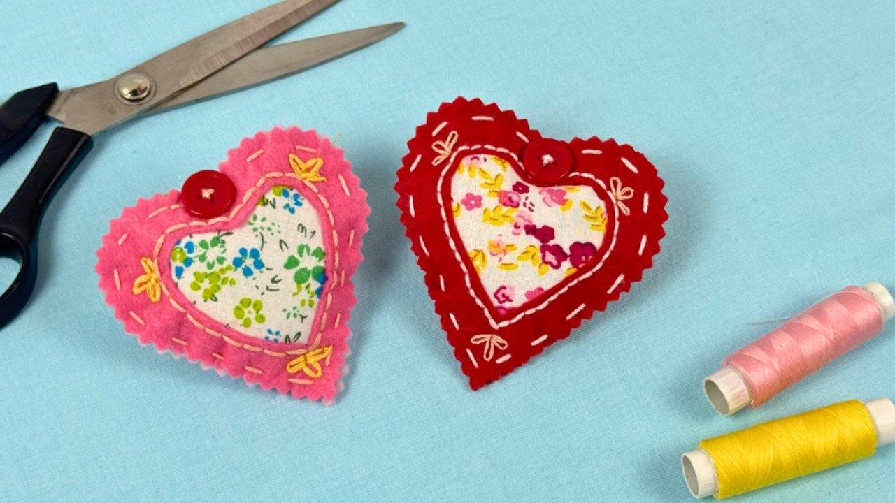 Easy fabric hearts, a pink and a red felt heart with floral centres and white blanket stitch edges, with thread and scissors