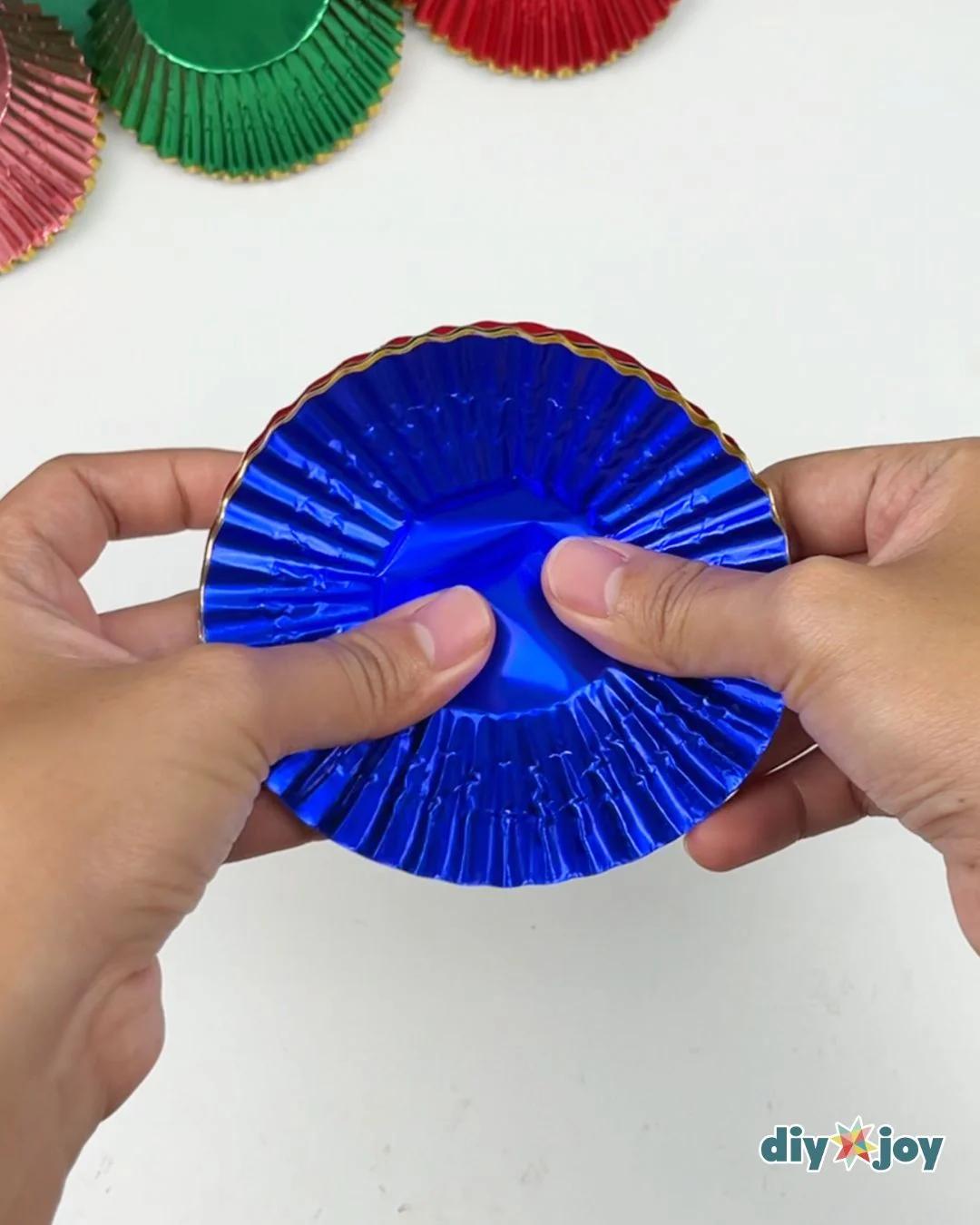 Easy Crafts - two hands opening up a blue metallic cupcake liner on a white table with red and green liners nearby