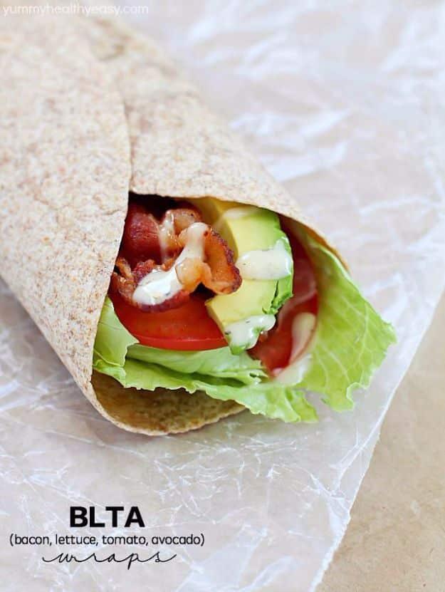 BLTA wrap with bacon, lettuce, tomato and avocado rolled in a tortilla and cut in half on a board on a wooden board