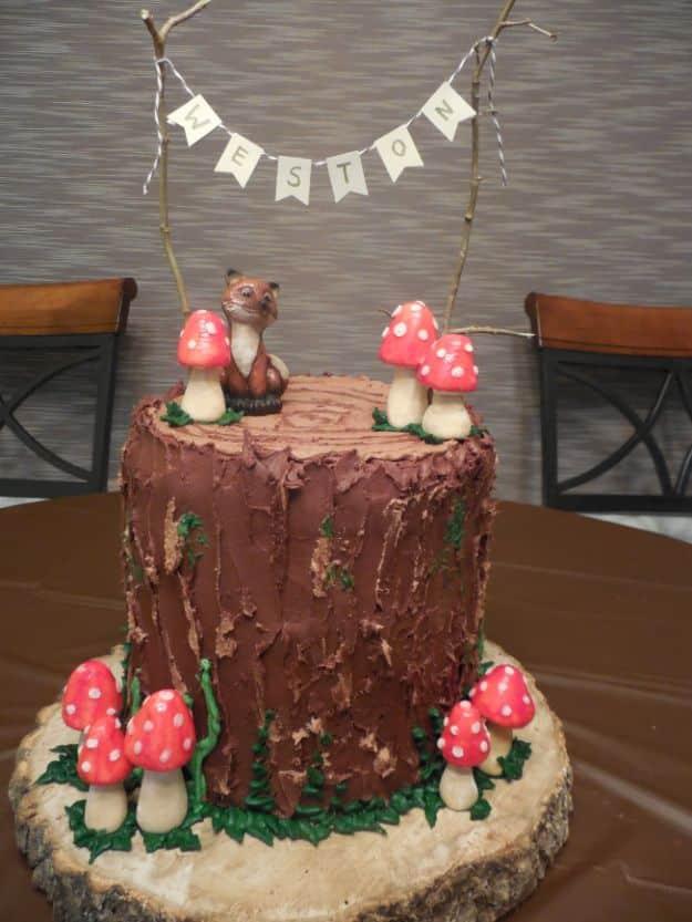 Tall chocolate log cake with bark texture, red toadstools, a squirrel topper and paper bunting on a wood slab