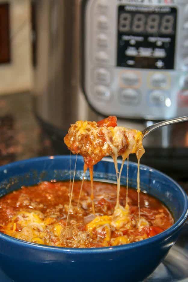 Quick keto chili in a blue bowl in front of an Instant Pot with melted cheese stretching from a spoon