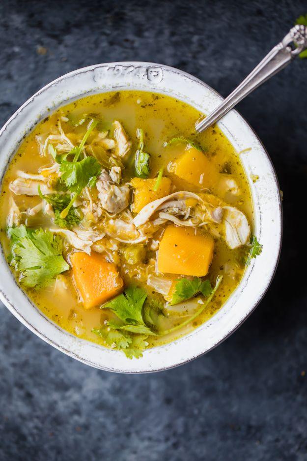 Butternut squash green chile chicken soup in a white bowl, golden broth with shredded chicken and squash cubes