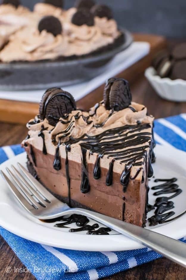 No bake chocolate cream pie slice on a white plate with whipped cream, mini Oreos and a chocolate drizzle