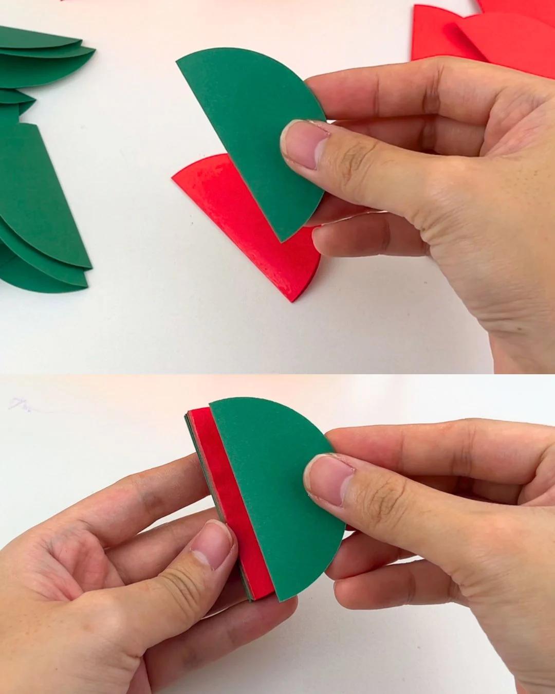 How to Make Paper Ornaments - a hand pressing a folded green half circle edge to edge against a red one, then gluing along its straight edge