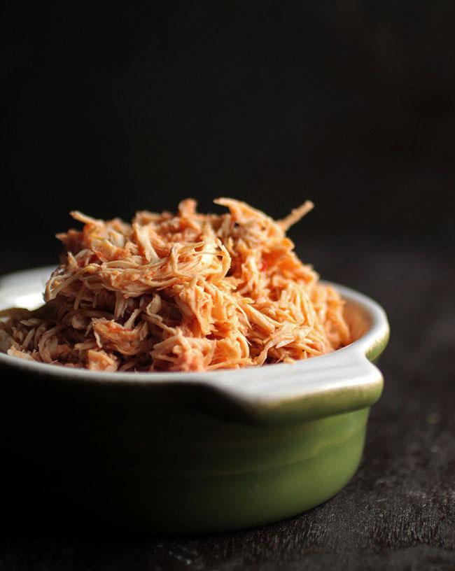 Shredded slow cooker salsa chicken piled high in a small green ceramic dish against a dark background
