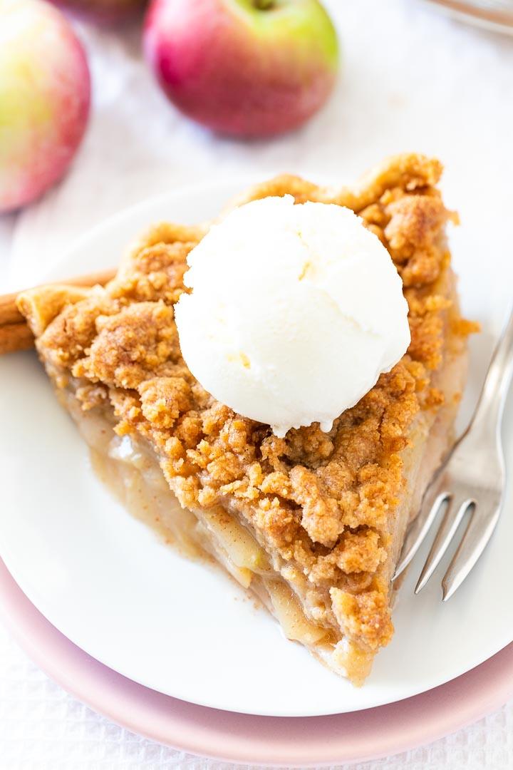 Apple crumble pie slice with a thick buttery crumb topping and vanilla ice cream melting over the apples