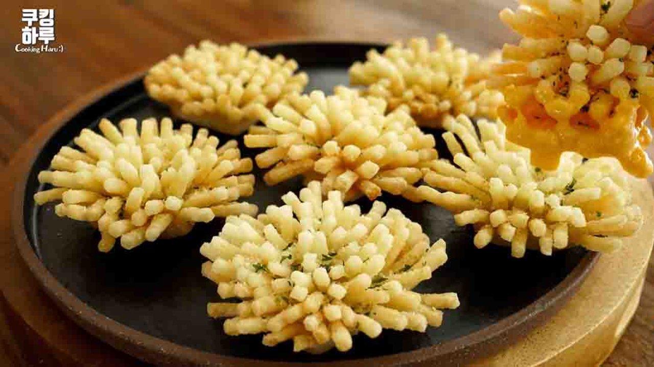 Deep fried potato flowers with spiky golden petals on a black plate, one being lifted with cheese dip