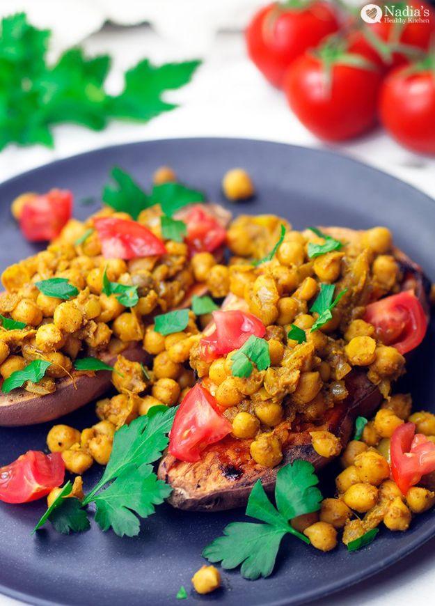 Baked sweet potato split open on a navy plate, loaded with garam masala chickpeas, tomatoes and coriander