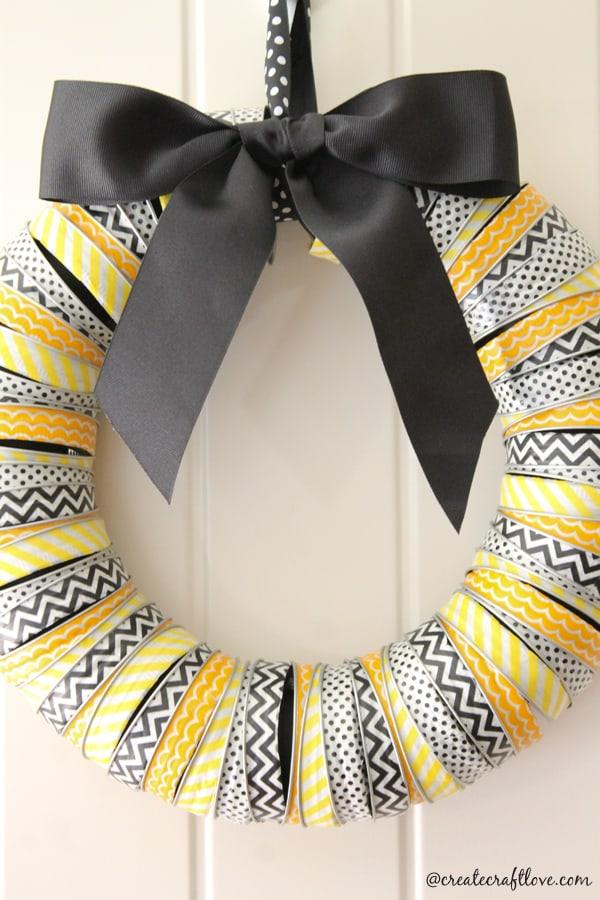 Black, white and yellow washi-tape-wrapped canning rings forming a Halloween wreath with a wide black ribbon bow