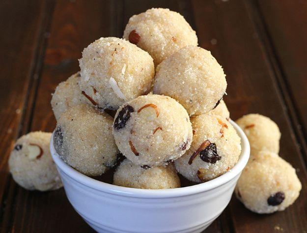 Pile of round rava coconut laddu studded with raisins in a small white bowl on a dark wooden table top