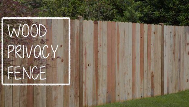 Wood privacy fence, a tall dog ear board fence in mixed natural cedar tones running along a lawn beside dark shrubs