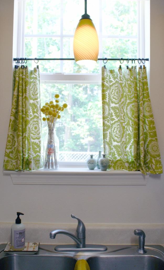 DIY cafe curtains in green and white floral fabric clipped to a rod across the lower half of a kitchen window above a sink