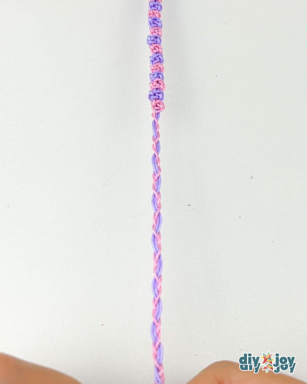 A beginner macrame bracelet tutorial step, with the folded cords tied and taped to the table ready for knotting