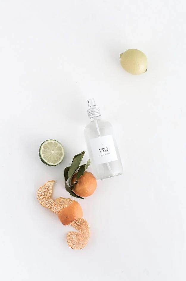 White room spray bottle photographed with lime, orange and dried citrus slices scattered on a plain background